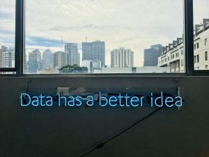 A neon sign reading 'Data has a better idea'. The sign is in a room that has a window with a cityscape view.