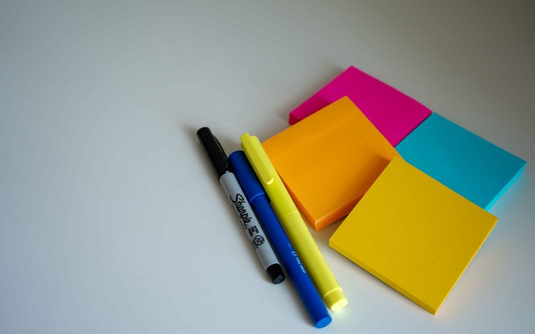 Stock image of four pads of coloured sticky notes on a white table, with three textas sitting alongside