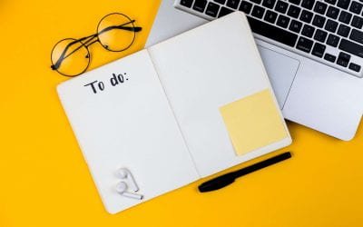 A paper planner open to a page titled 'to do'. The planner is arranged with a laptop, airpods, glasses and pen on a yellow background.