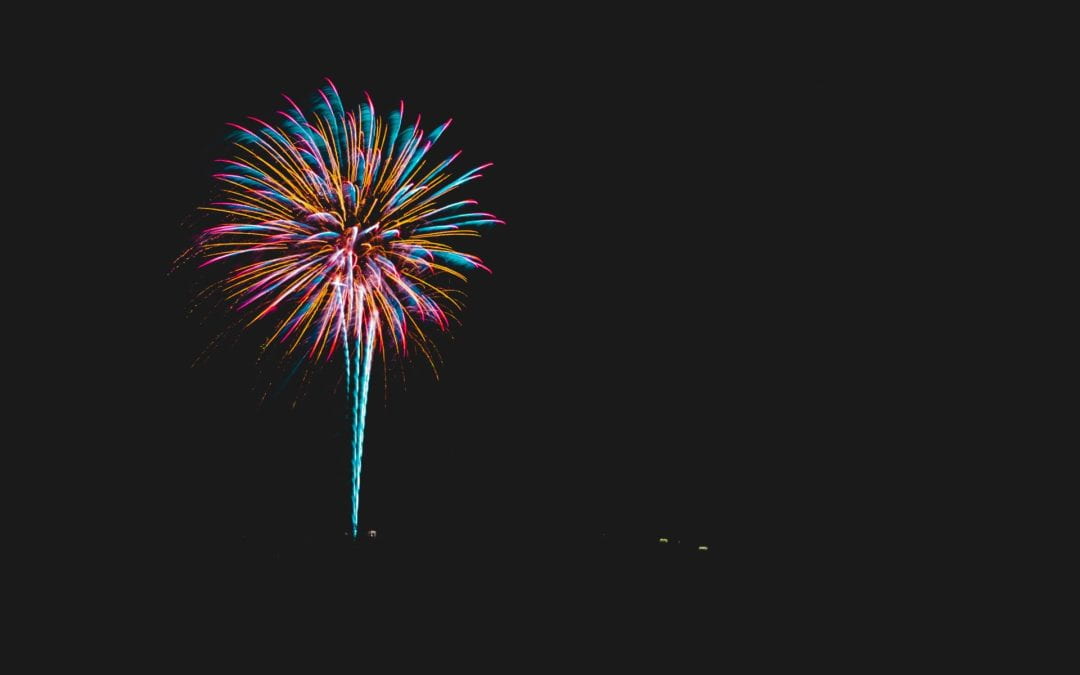 A single vivid pink, blue and gold firework against a dark sky