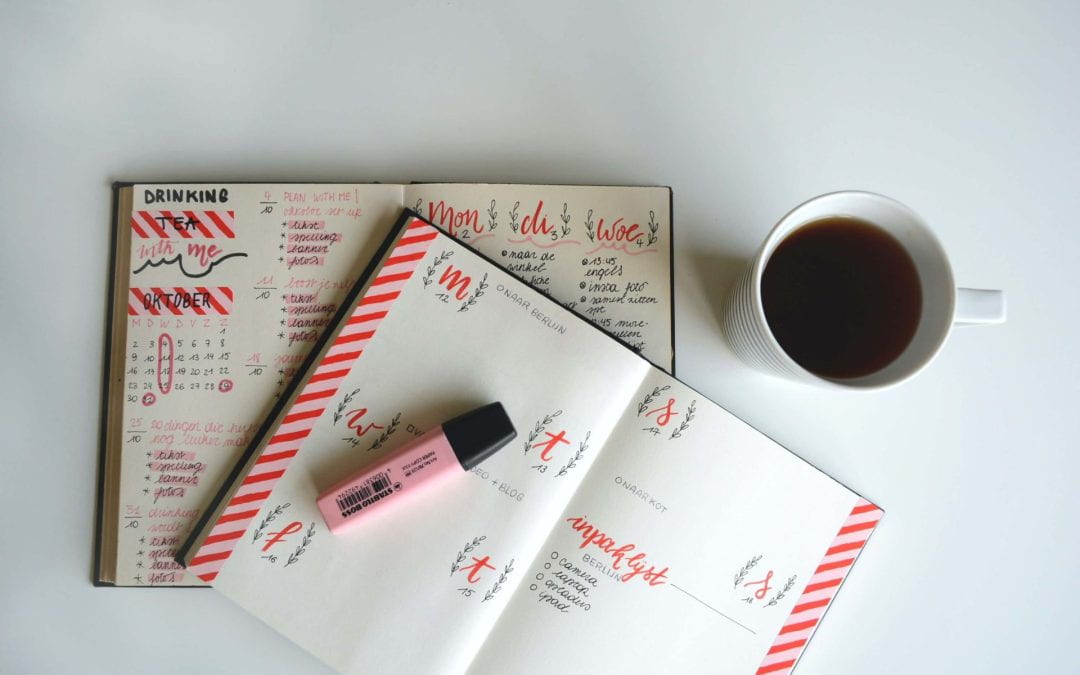 An overhead shot of two bullet journal-type planners with handwritten dates. A pink highlighter is sitting on top and a cup of coffee is sitting to the side.