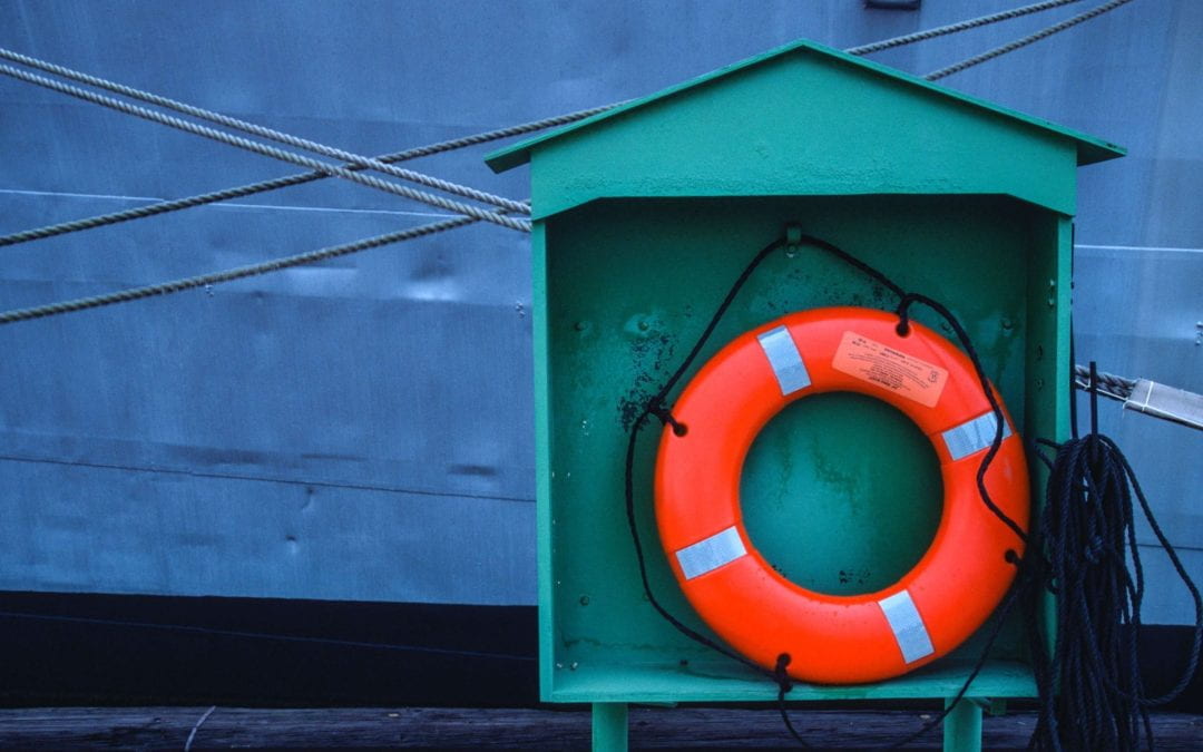 A bright orange life preserver in teal wooden housing, with a vaguely industrial maritime style backdrop.