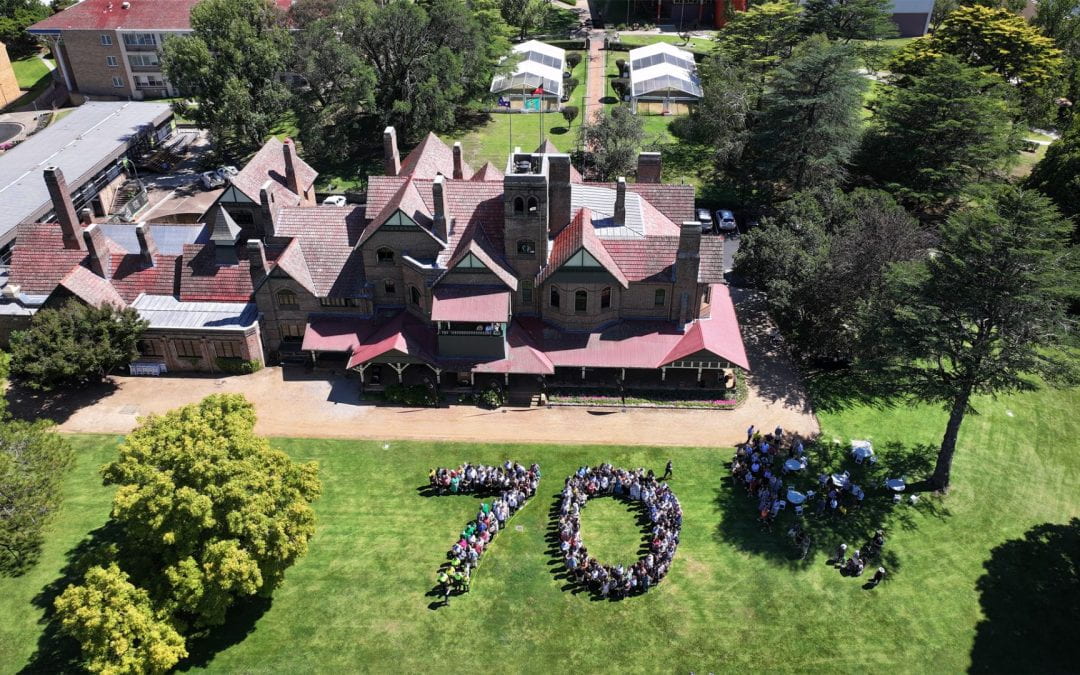UNE celebrating it's 70th birthday with an overhead shot of staff standing together to form the numbers seventy on the lawns of Boolimibah.