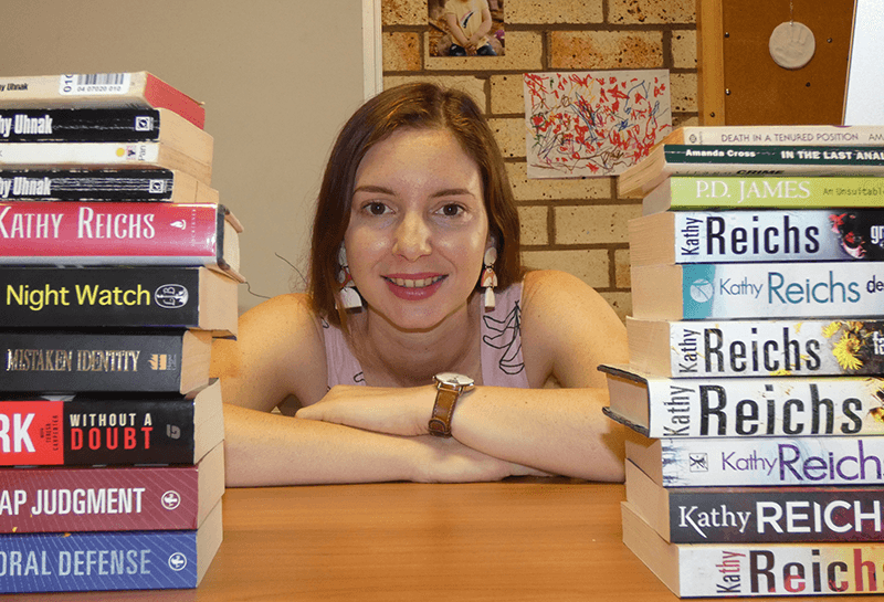 Portrait image of Lili Paquet at a desk among piles of crime fiction books