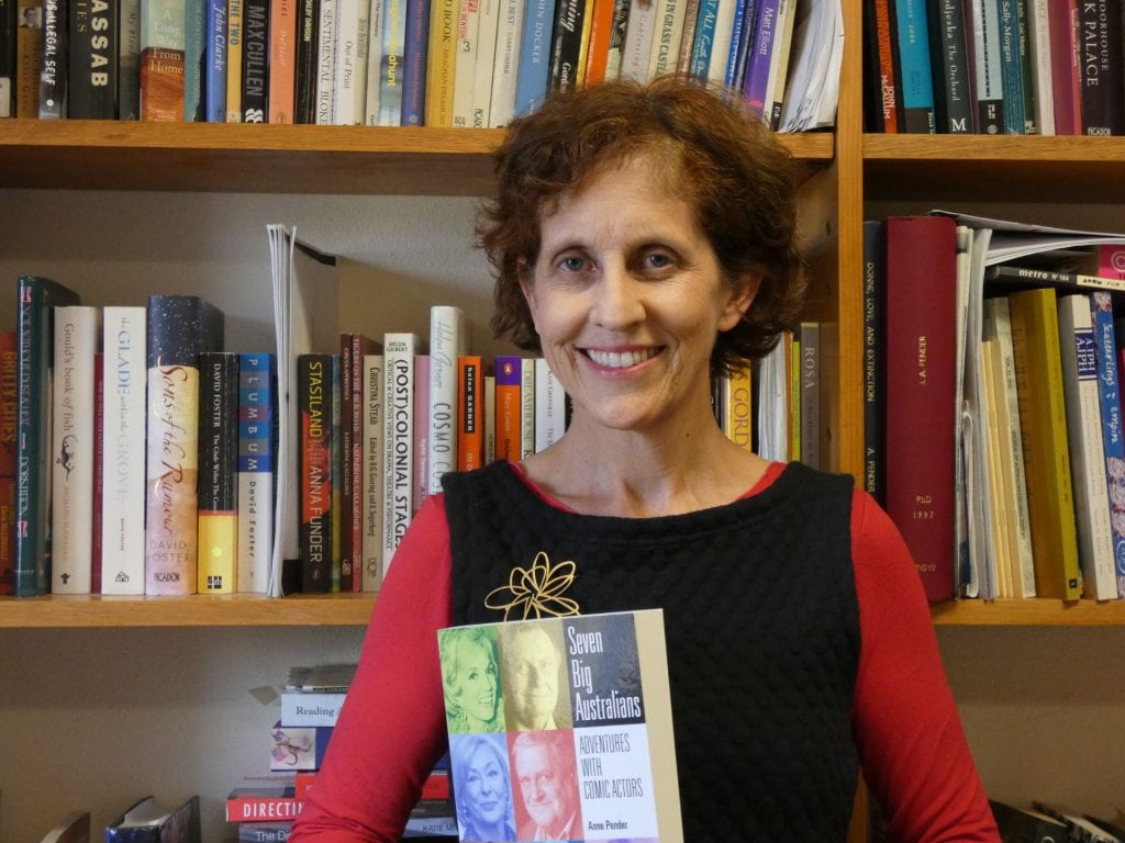 Anne Pender in front of a bookcase holding her newly released book on Australian comedians