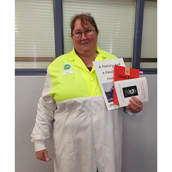 UNE history graduate Carol Corless at work in hi-vis overalls holding labour history brochures