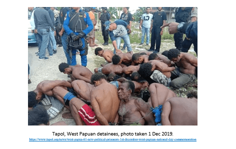 Group of West Papuan detainees, tied up and kneeling before police and onlookers