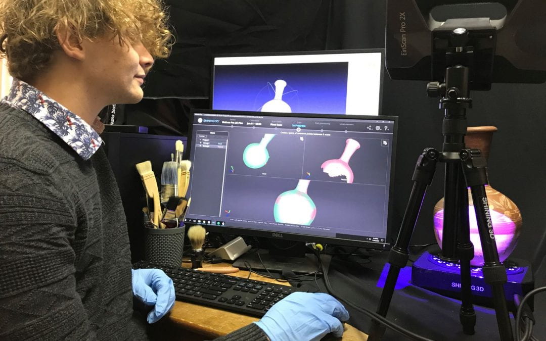 UNE history graduate Jackson Shoobert wears gloves in a computer lab environment as he prepares to upload images of an ancient vase artefact onto an online platform seen on a computer screen.