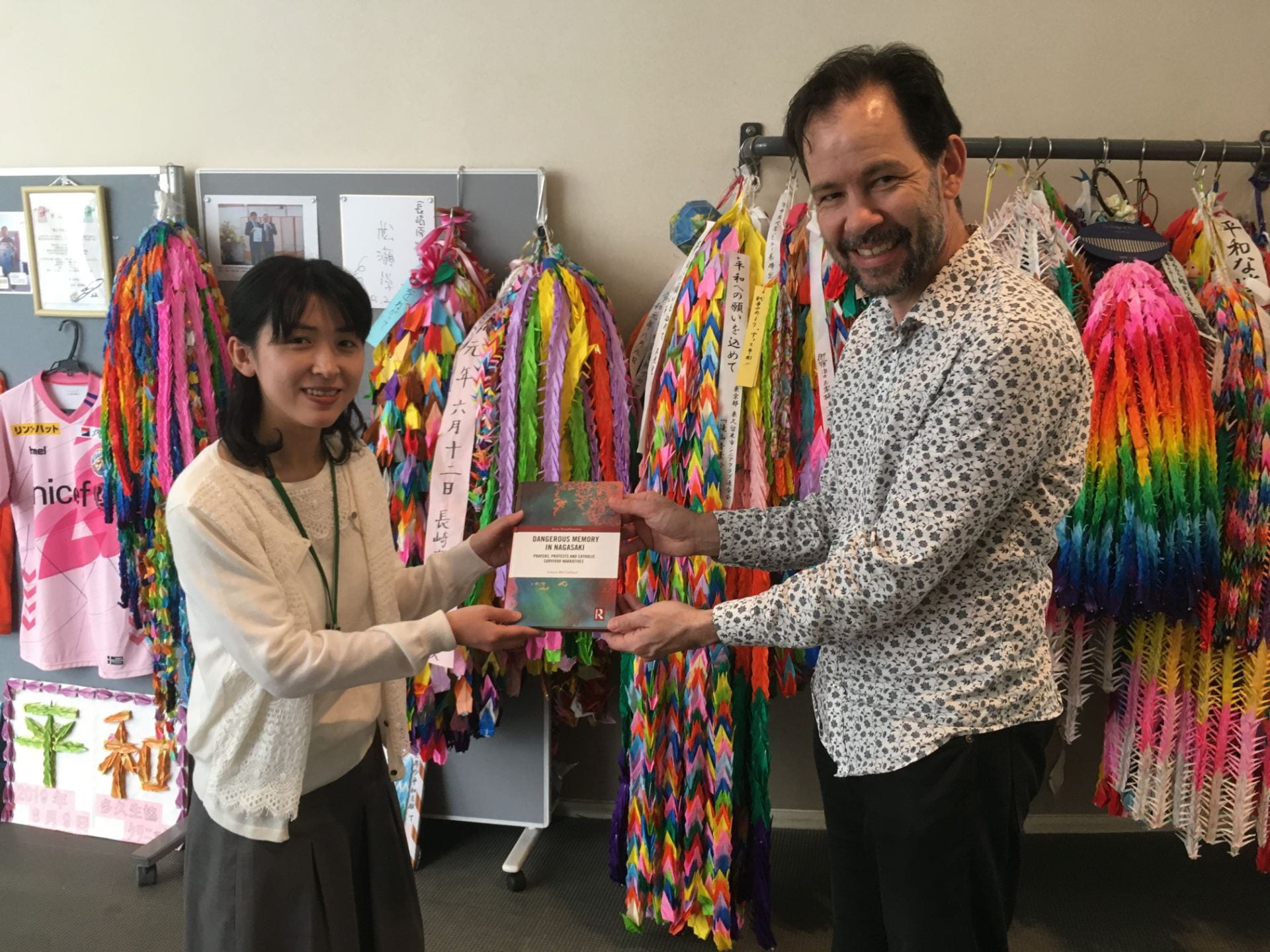 Dr Gwyn McClelland passes a book of of stories from the bombing of Nagasaki to a Japanese woman in Nagasaki, 2019.