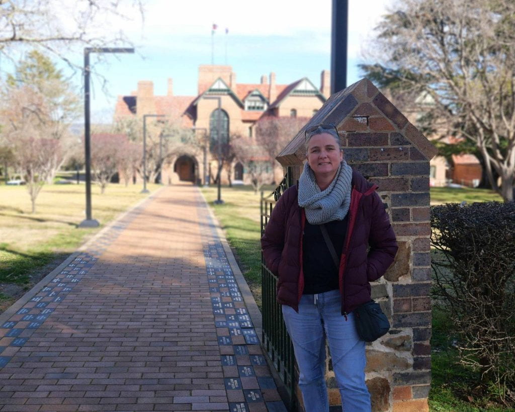 UNE archaeology PhD candidate stands in front of UNE's historic administrative building, Booloominbah House