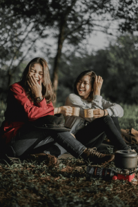 Two women laughing sitting near a camping scene