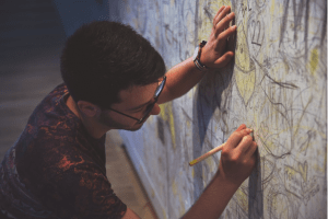 Man wearing glasses drawing on a graffiti wall