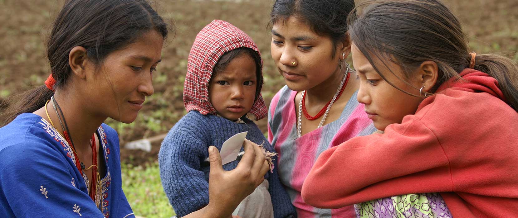 Three Nepalese women with a child, looking at a photograph, in a rural setting.