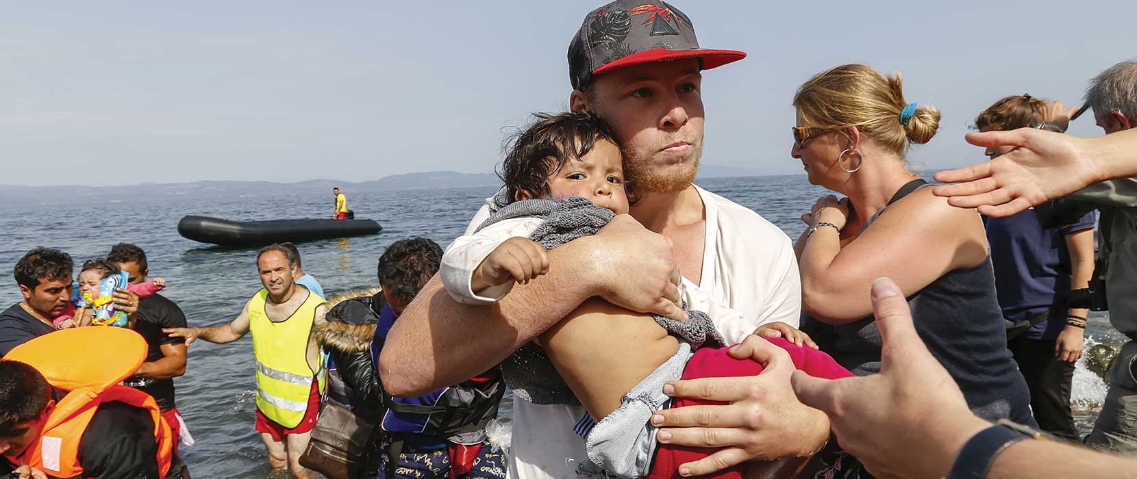 Refugees arriving in Greece on boats with people carrying young children from the sea onto land.